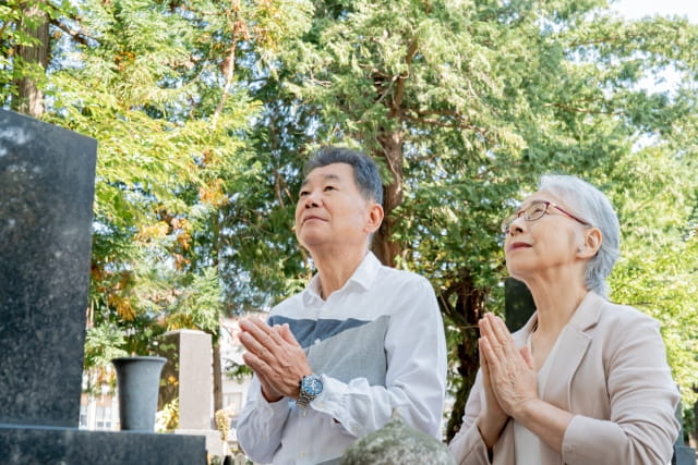 墓前で手を合わせる高齢の夫婦